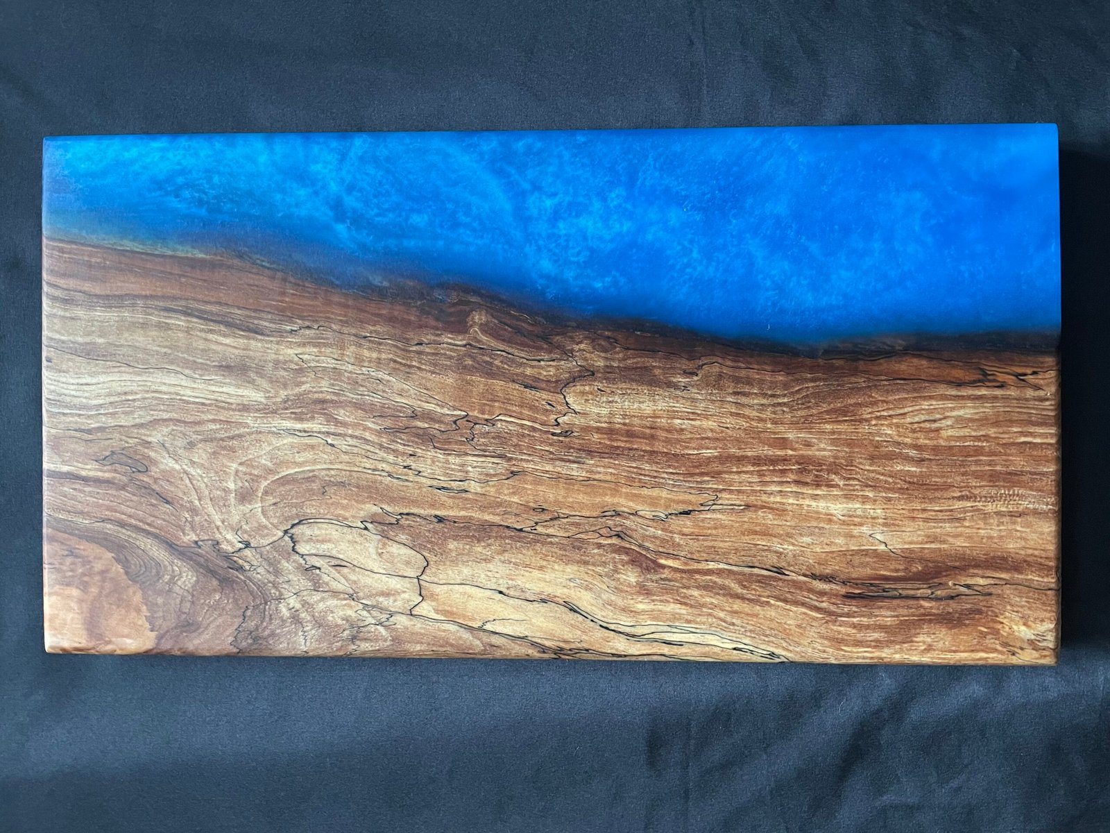 A spalted curly live edge applewood and blue resin charcuterie board.